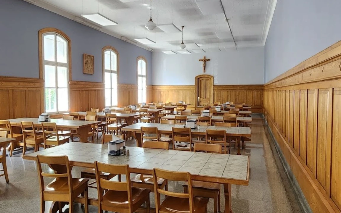 Salle à manger avec tables et chaises en bois, murs lambrissés et un crucifix au fond de la pièce